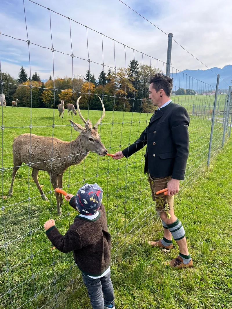 Christian Heiß füttert mit einem Kind einen Hirsch am Gehegezaun